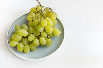 a branch of green sweet grapes lies on a plate, on a white background