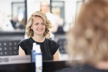 Woman with an evening hairstyle in a beauty salon sits in front of mirror and smiles. Creating an image for celebrations concept