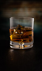 Glass of Kentucky Bourbon on rocks reflecting on black stone surface and refracting colorful wooden background.