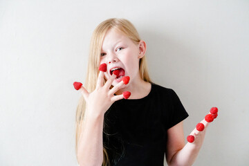 Girl with a big raspberry on her fingers. Happy child eating berries