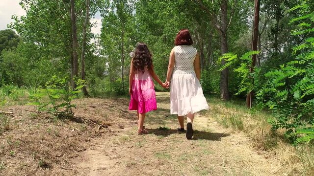 Dos j&oacute;venes hermanas de la mano pasean por bosque de espalda y un dron las sigue