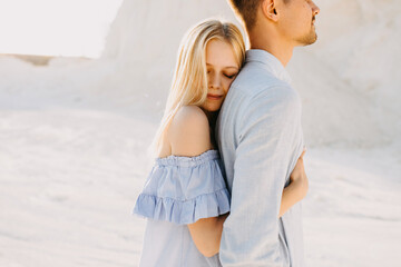 Young romantic couple outdoors. Woman hugging man from behind, with eyes closed.