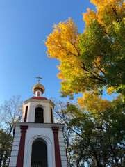 Orthodox church in the autumn colorful forest. Bright yellow leaves of the tree lit by the sun. Blue sky. Copy space. Religion concept.