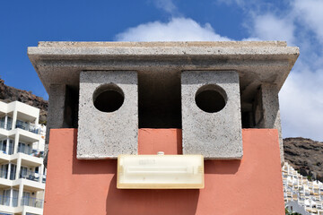 Modern Concrete Air Vent & Light on Roof of Hotel with Blue Sky-White Clouds and Background Buildings 