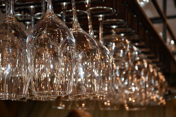 Abstract background of large glass wine glasses hanging on the bar. A lot of highlights from the lamps on the surface of the glass. Soft focus, blurred background.
