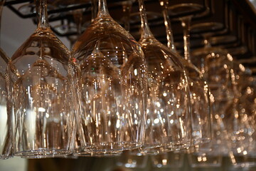 Abstract background of large glass wine glasses hanging on the bar. A lot of highlights from the lamps on the surface of the glass. Soft focus, blurred background.