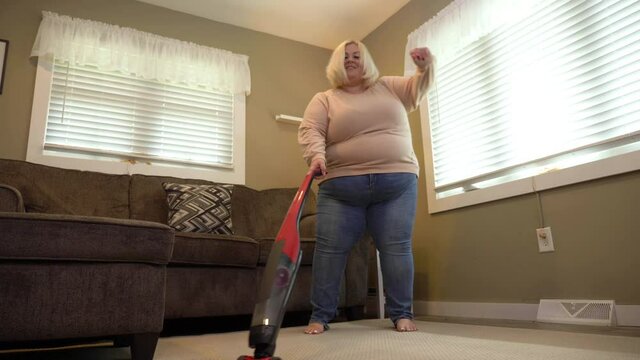 A low angle view of a woman vacuuming the living room carpet while dancing. Shot at 60fps for optional slow motion use.  	
