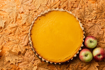 top view of thanksgiving pumpkin pie with apples and autumnal foliage on wooden background