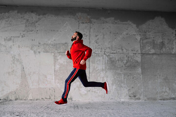 Side view of attractive fit sportsman in red tracksuit running fast.