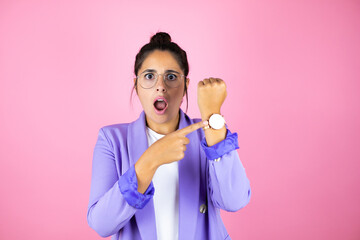 Young beautiful business woman over isolated pink background surprised and pointing his watch...