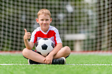Boy posing with soccer ball on green grass. Sports training in the field. Kid sport online concept