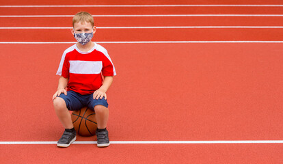 Obraz premium School kid with mask and basketball ball in a physical education lesson. Safe back to school during pandemic concept. Social distancing to fight COVID-19