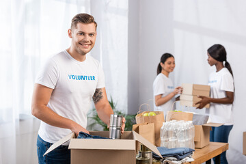 Selective focus of volunteer putting tin cans in carton box in charity center