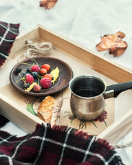 Autumn cozy composition. A cup of coffee, autumn fruits and a warm blanket on a wooden tray on a white bed. Morning coffee.