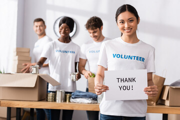 Selective focus of asian woman looking at camera while holding card with thank you lettering in charity center