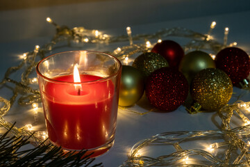 Red christmas candle, burning candle fire on a table with holiday garland and pine tree decorations and balls, festive christmas mood