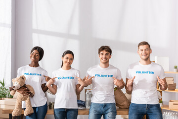 Multiethnic volunteers pointing with fingers at t-shirts and showing like in charity center