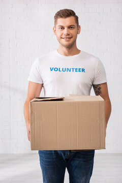 Volunteer In White T-shirt Holding Cardboard Package In Charity Center