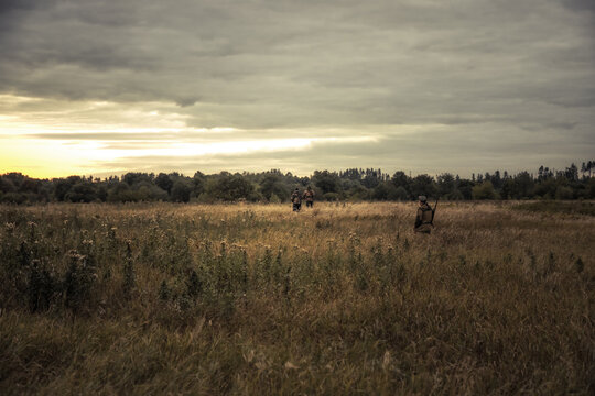Hunters men during hunting standing in rural field and looking into the distance forest at beautiful sunset as hunting lifestyle