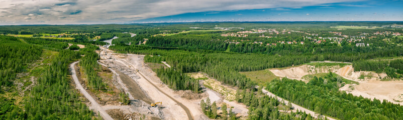 Fototapeta na wymiar Panorama drone photo on construction of new highway and bridge over Umea river - many heavy industrial machines work together - dump trucks, bulldozer and excavator. Construction site and Umea city