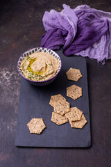 Obraz na płótnie Canvas Eggplant Hummus in a Purple Bowl on a Black Board and Background with Crackers