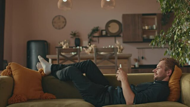 A man lies on a sofa and uses a smartphone. Cozy Living Room