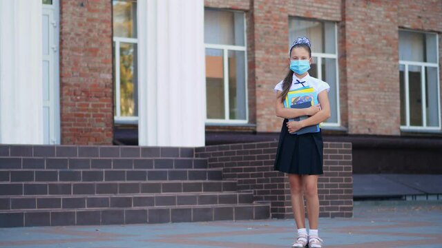 outdoors. schoolgirl, teenage girl, in medical protective mask, with books in her hands, on background of school building. Back to school after covid19 outbreak.