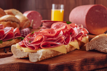 Mortadella sandwich with orange juice and bread on wood cutting board