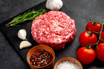 Raw beef burger cutlets with rosemary and spices on a slate board on a concrete background