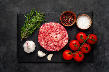 Raw beef burger cutlets with rosemary and spices on a slate board on a concrete background