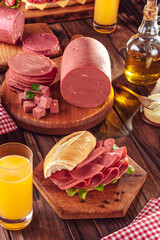 Mortadella sandwich with orange juice, butter, slices and piece of mortadella on wood background