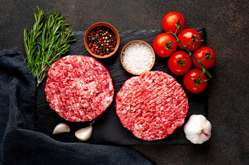 Raw beef burger cutlets with rosemary and spices on a slate board on a concrete background