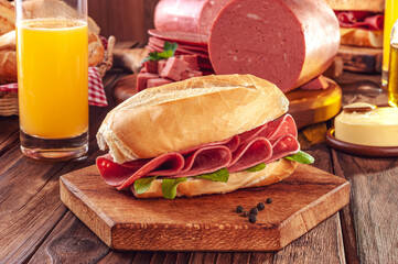 Mortadella sandwich with orange juice, butter and piece of mortadella on wood background - obrazy, fototapety, plakaty