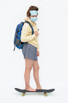 Vertical photo of the barefoot female student on the skate board with the disposable masks of the face over the white background