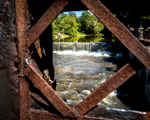 View of River and Waterfall Through Rusty Metal Fence
