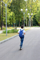 a handsome stylish and young schoolboy in a white shirt, blue tie and a backpack with a scooter on a street. back view