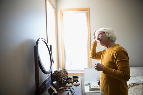 Senior woman fixing hair in mirror in bedroom