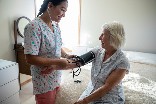 Smiling home caregiver checking blood pressure of senior woman on bed