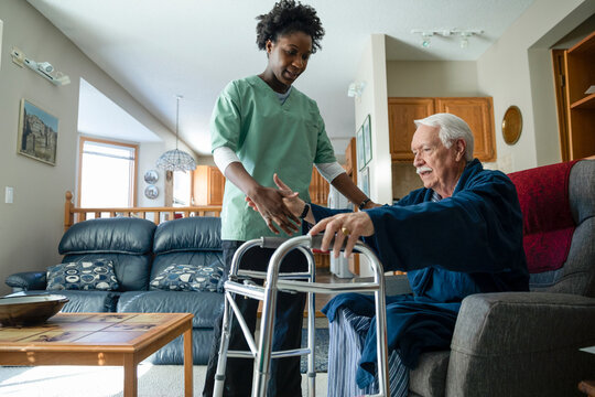 Home caregiver helping senior man with walker in living room