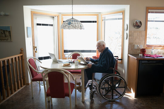 Senior man in wheelchair eating breakfast and reading newspaper at din