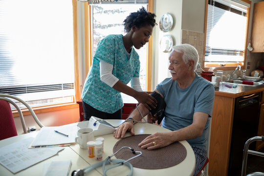 Home caregiver checking blood pressure of senior man at dining table