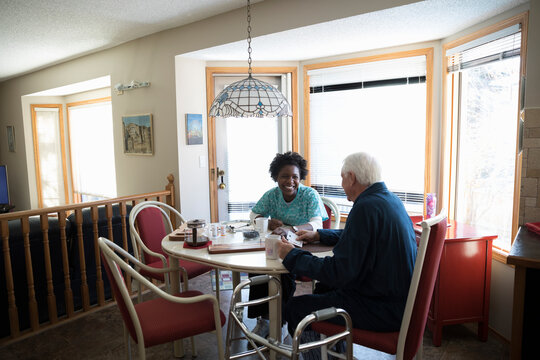 Home caregiver and senior man playing cards at dining table