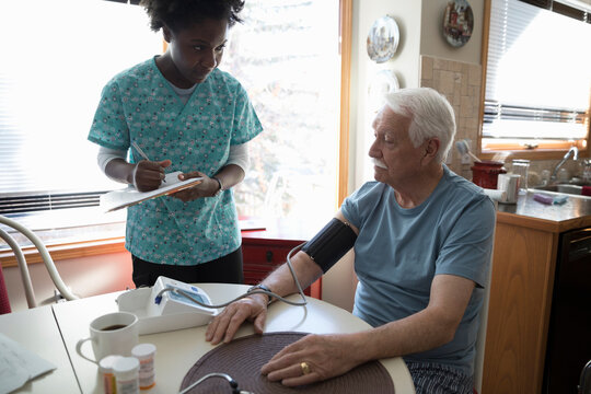 Home caregiver checking blood pressure of senior man at dining table