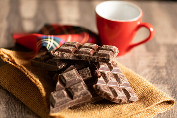 Broken chocolate pieces on wooden background. Selective focus.