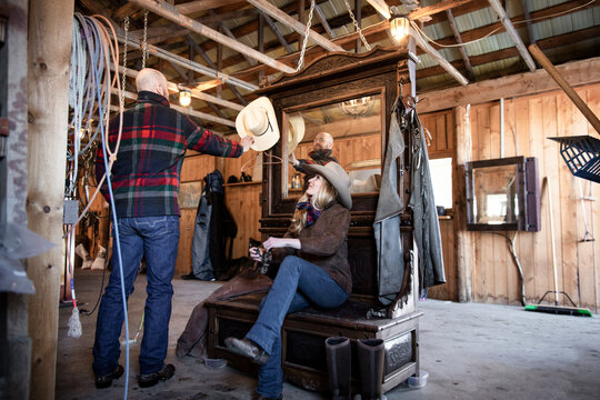 Rancher couple putting on cowboy boots and cowboy hat in stable