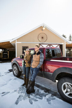 Ranchers drinking coffee at truck in snow outside barn