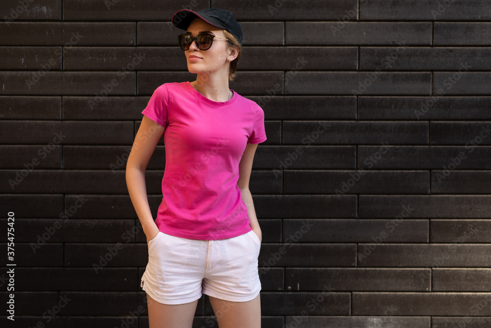 Wall mural Beautiful woman in blank pink t-shirt standing against brick wall wearing sunglasses