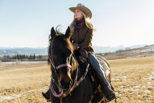 Female rancher horseback riding on sunny ranch