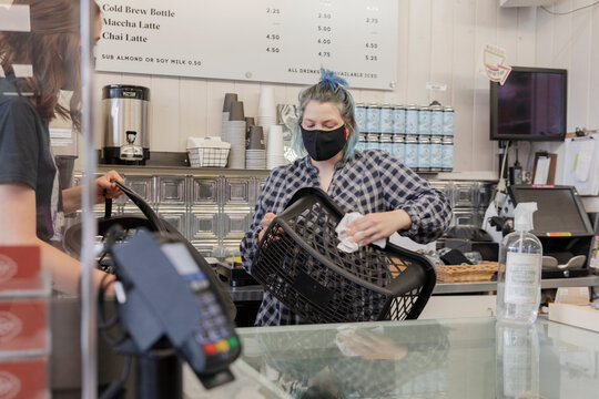 Female worker in face mask sanitizing shopping basket in cafe