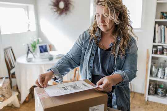 Female Artist Placing Shipping Label On Package In Home Art Studio